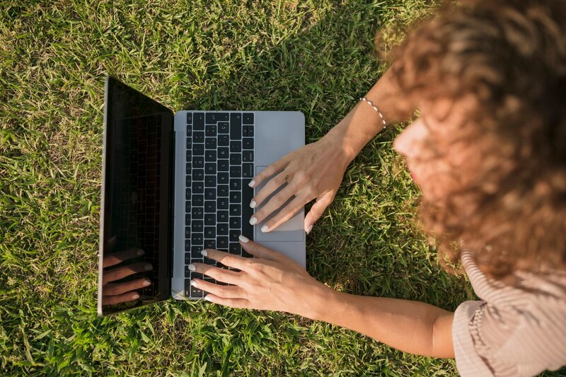 A woman sitting on grass, using her laptop.